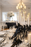 Wesele w stylu black tie z czarnymi krzesłami Elegancka sala weselna z czarnymi krzesłami z tiulem, jasnymi stołami i kryształowym żyrandolem.