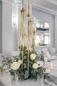 Złote świeczniki i eukaliptus – dekoracja stołu weselnego glamour Wysokie złote świeczniki z białymi świecami otoczone eukaliptusem i białymi różami.