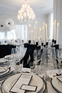 Wesele w stylu black tie z czarnymi stołami Elegancka sala weselna z czarnymi stołami, jasnymi kompozycjami kwiatowymi i kryształowym żyrandolem.